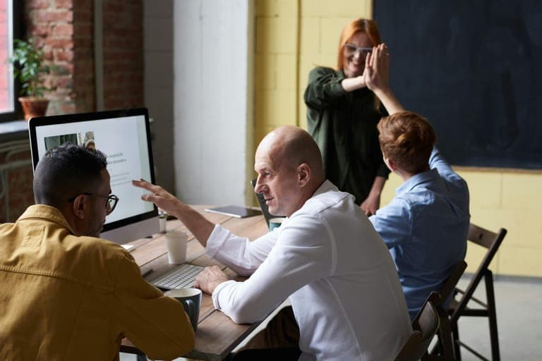 A group of four people engages in a discussion around a table in a bright, modern workspace.