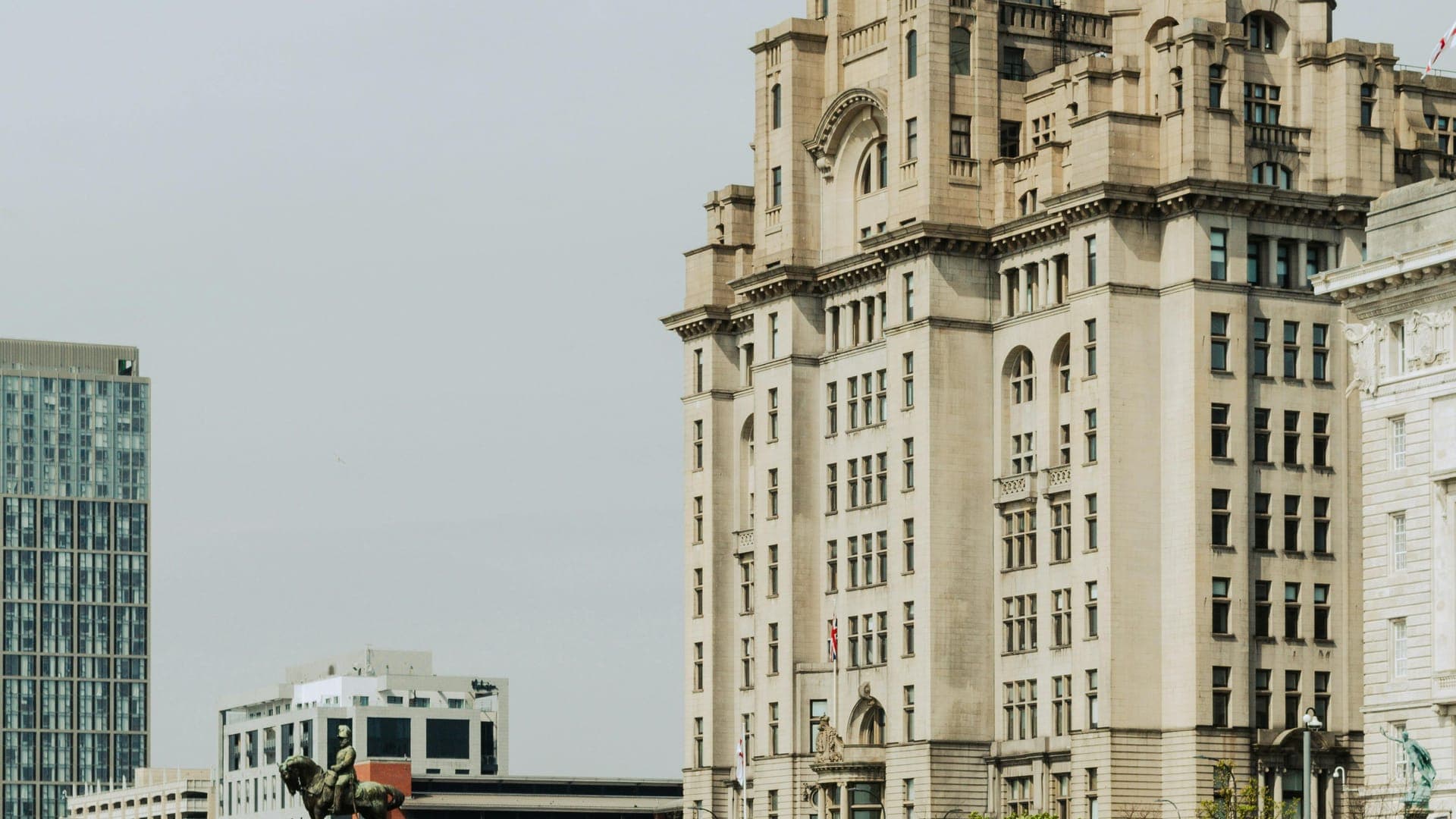 Historic clock tower building beside a paved walkway with people walking and sitting nearby.