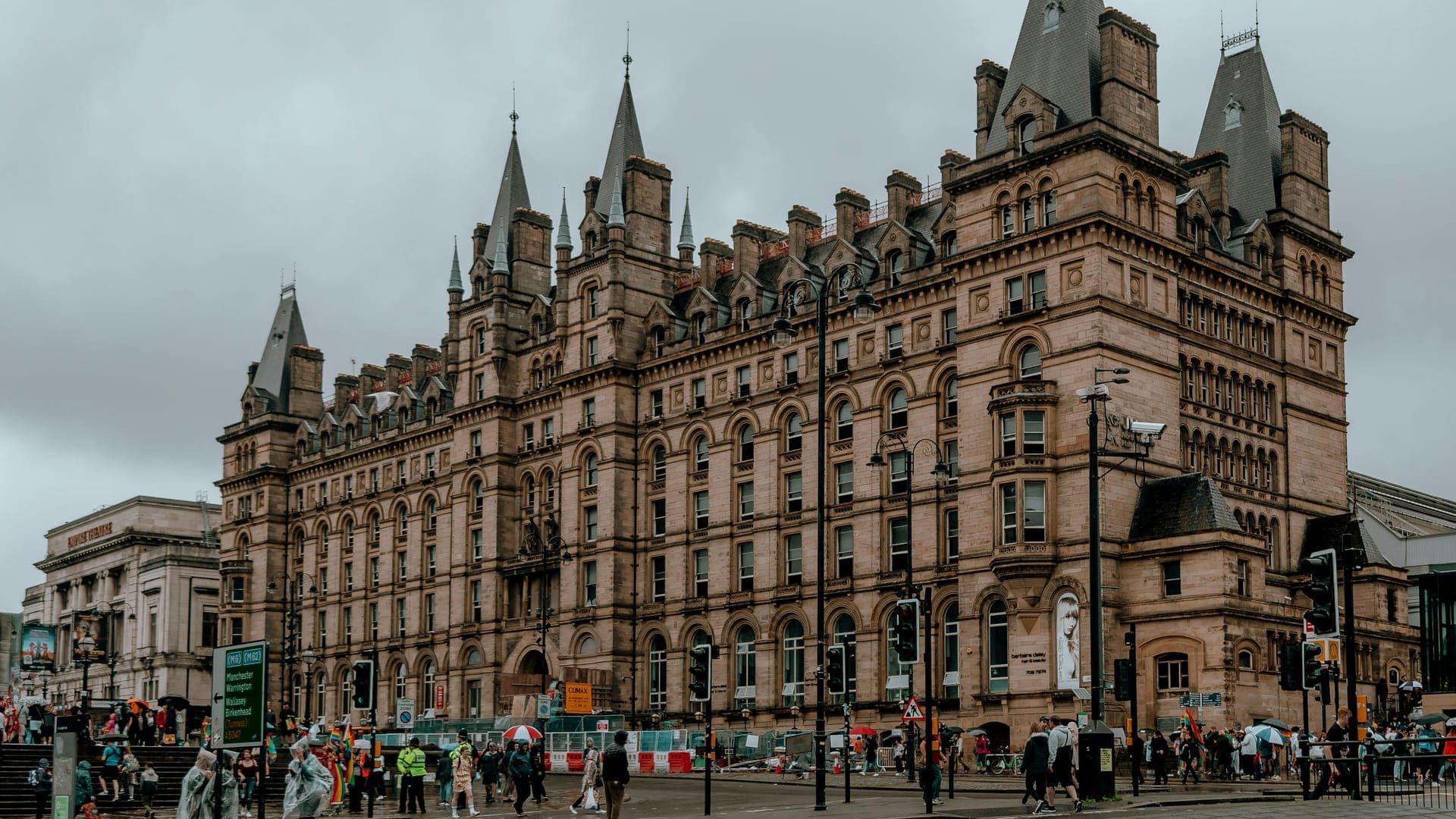 A large historical building with spires, surrounded by people and a cloudy sky.